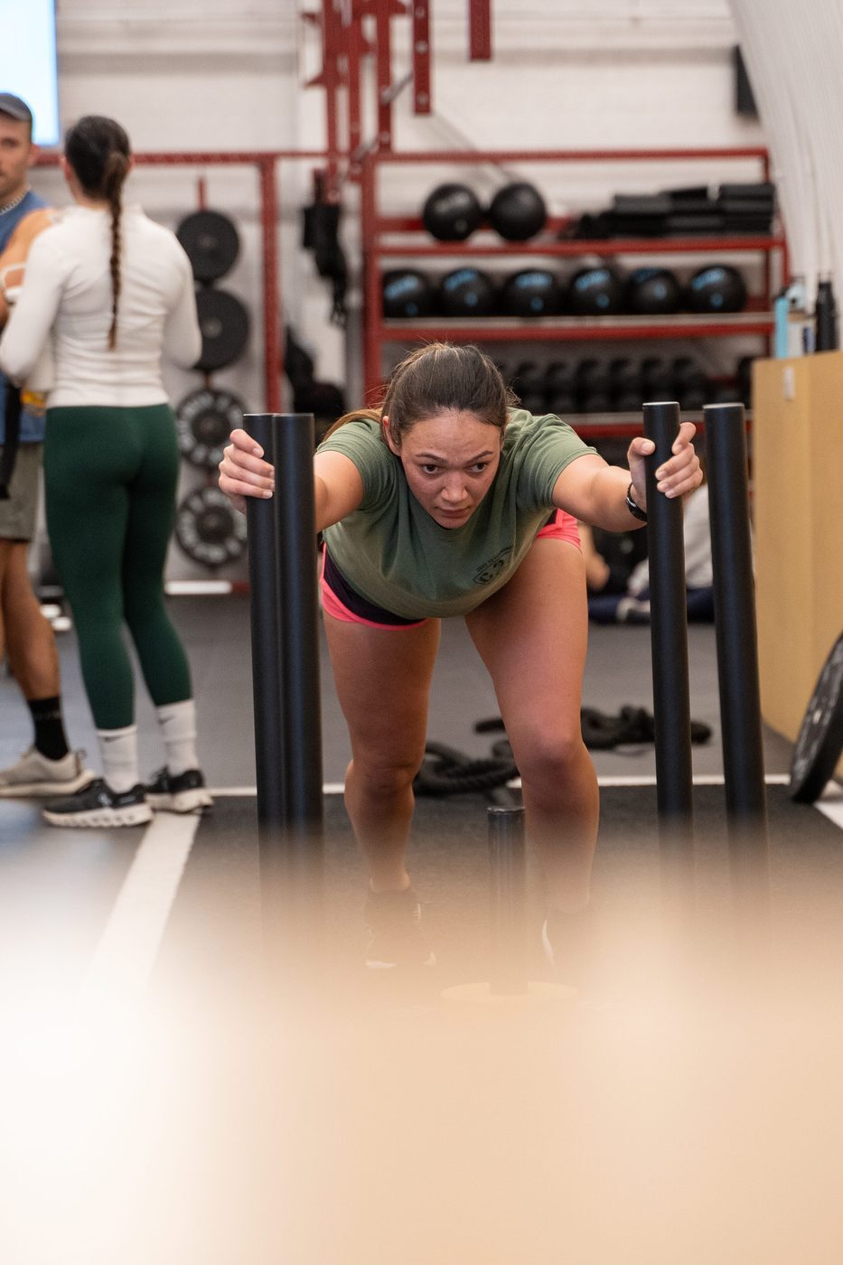 A Gymnasium member driving a sled low with straight arms during a coached HYROX session