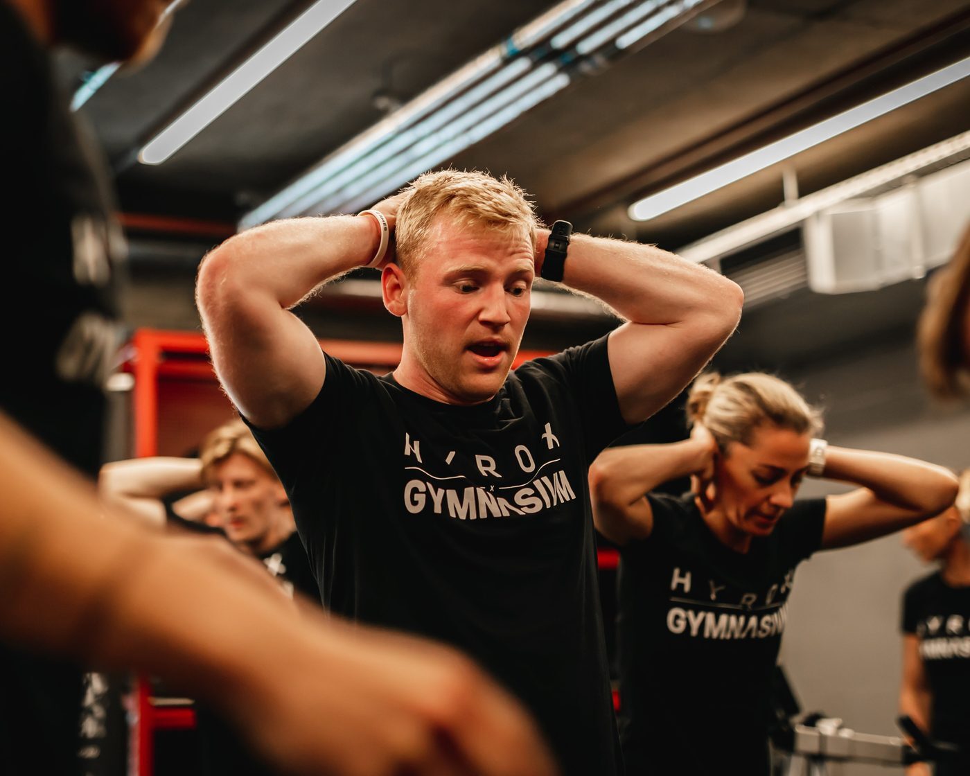 Gymnasium members in HYROX x Gymnasium T-shirts catching their breath between rounds of a coached session