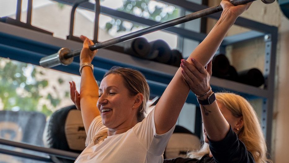 Member being coached through an overhead barbell lift